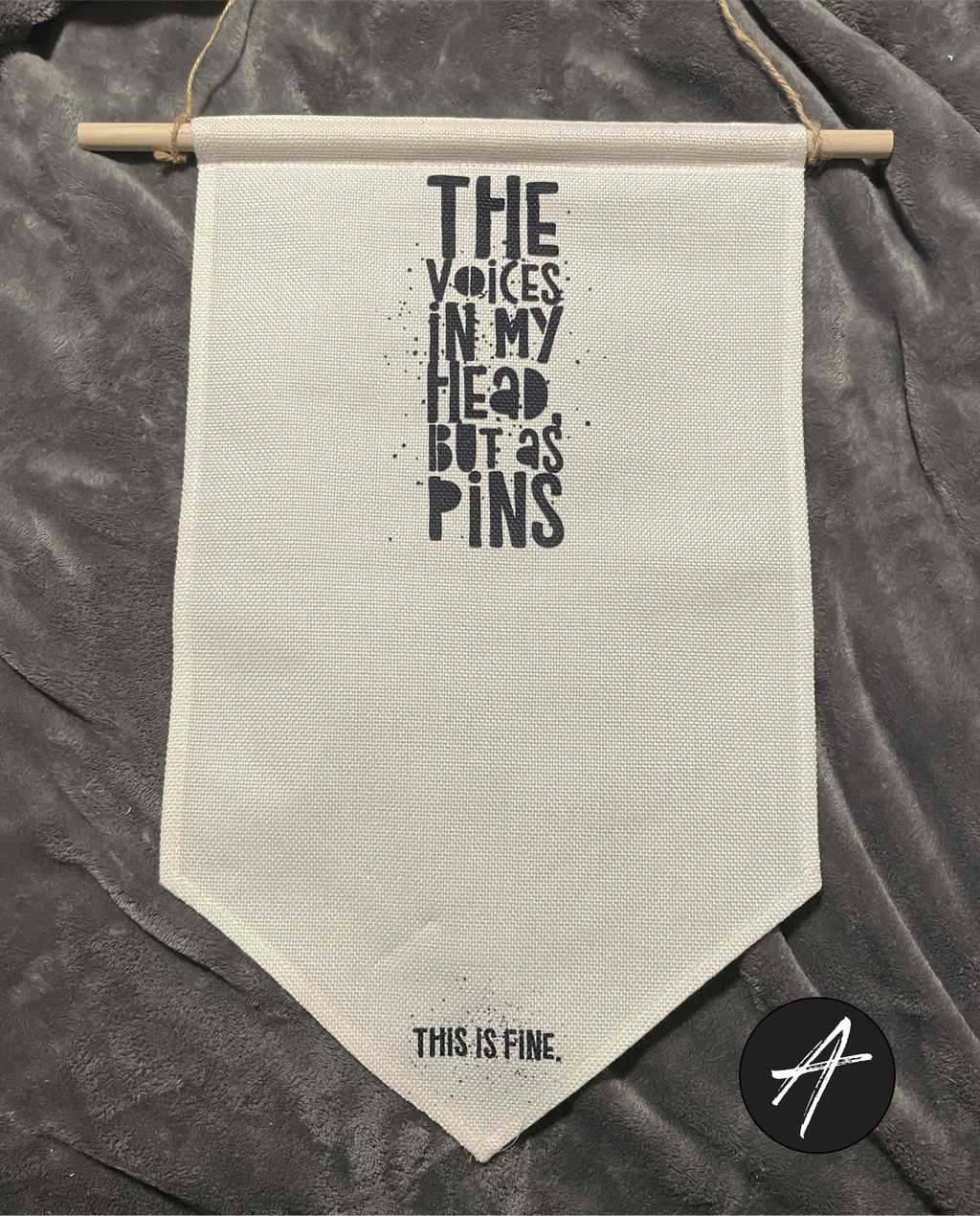 Vertical canvas pin holder. Distressed black text reads "The Voices In My Head, But As Pins." Small text at the bottom reads "This Is Fine."