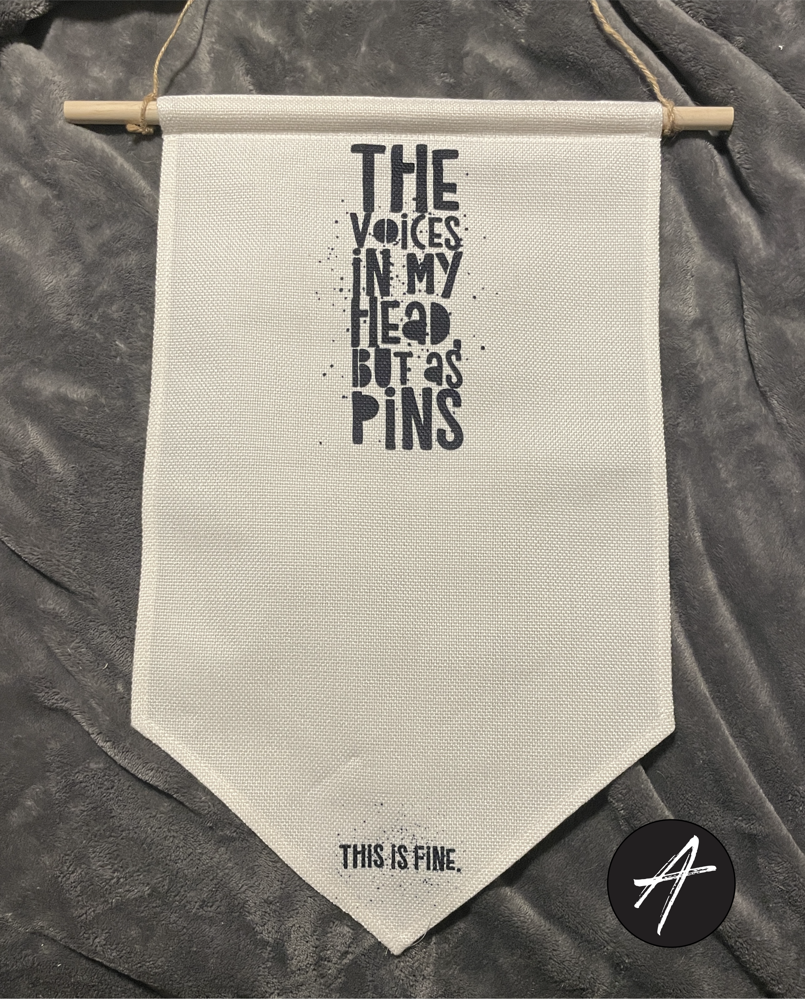 Vertical canvas pin holder. Distressed black text reads "The Voices In My Head, But As Pins." Small text at the bottom reads "This Is Fine."