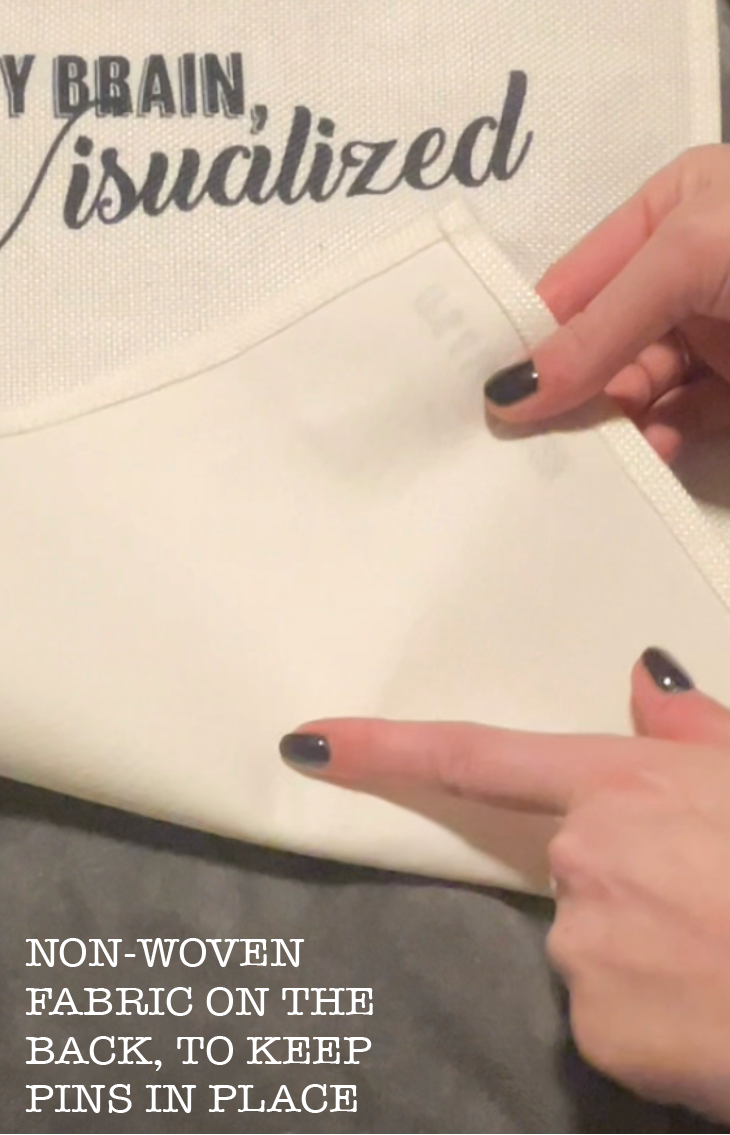 Close-up detail of the pin banner fabric. Hands lifting the corner of the banner to show the sturdy non-woven backing designed to keep pins and backings secure.