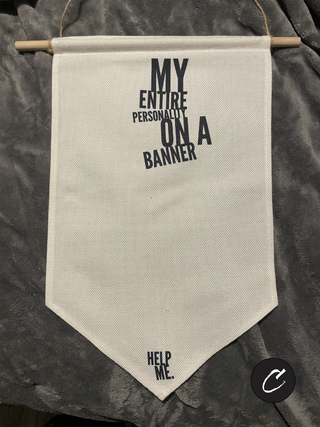 Cream canvas enamel pin display banner hanging on a wall. Black text reads "My Entire Personality On A Banner" in a bold font. Small text at the bottom point reads "Help Me."