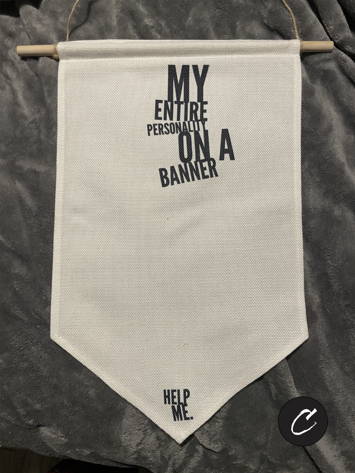 Cream canvas enamel pin display banner hanging on a wall. Black text reads "My Entire Personality On A Banner" in a bold font. Small text at the bottom point reads "Help Me."